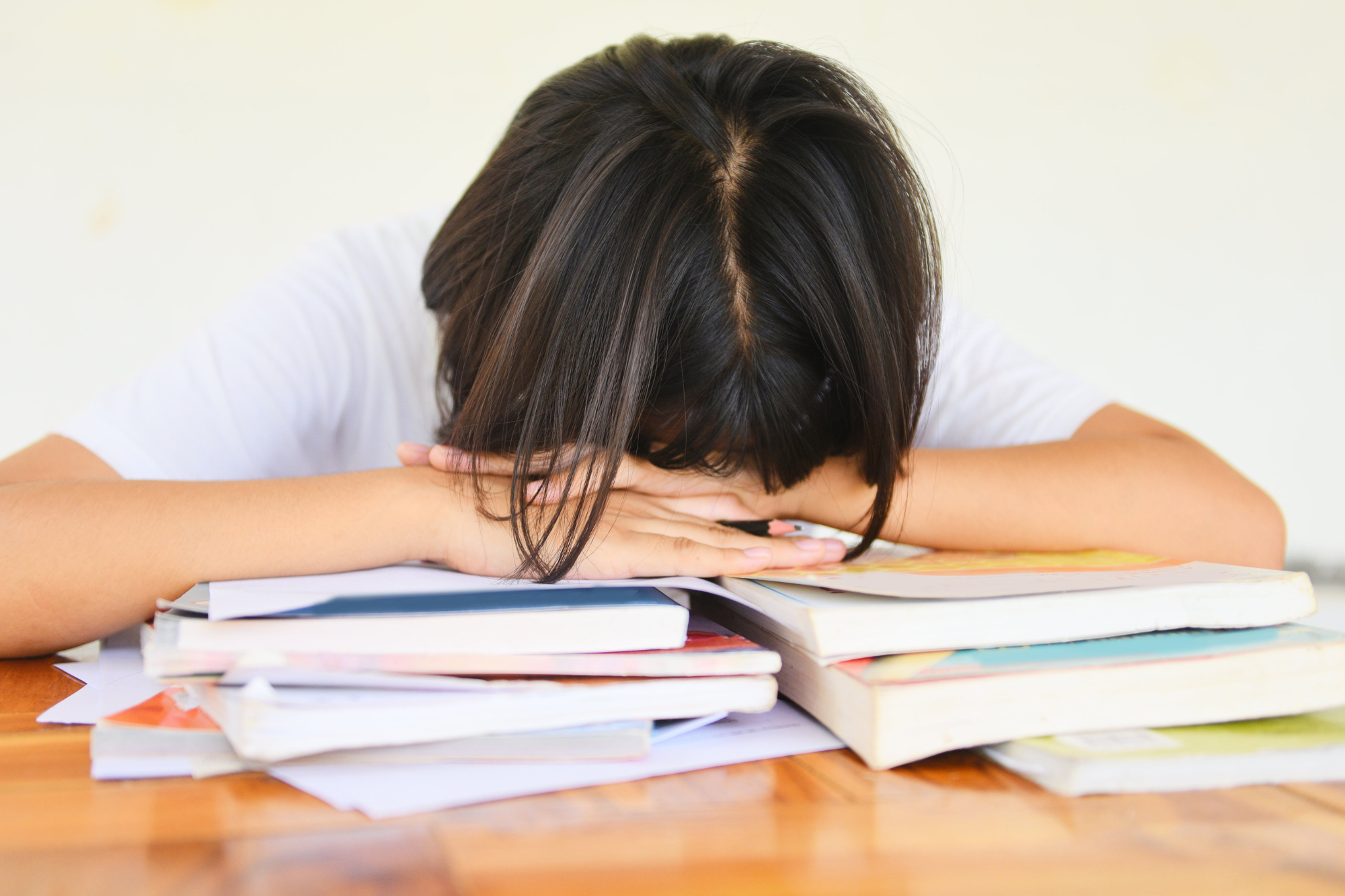 Stressed young person leaning on a pile of text books during exams.